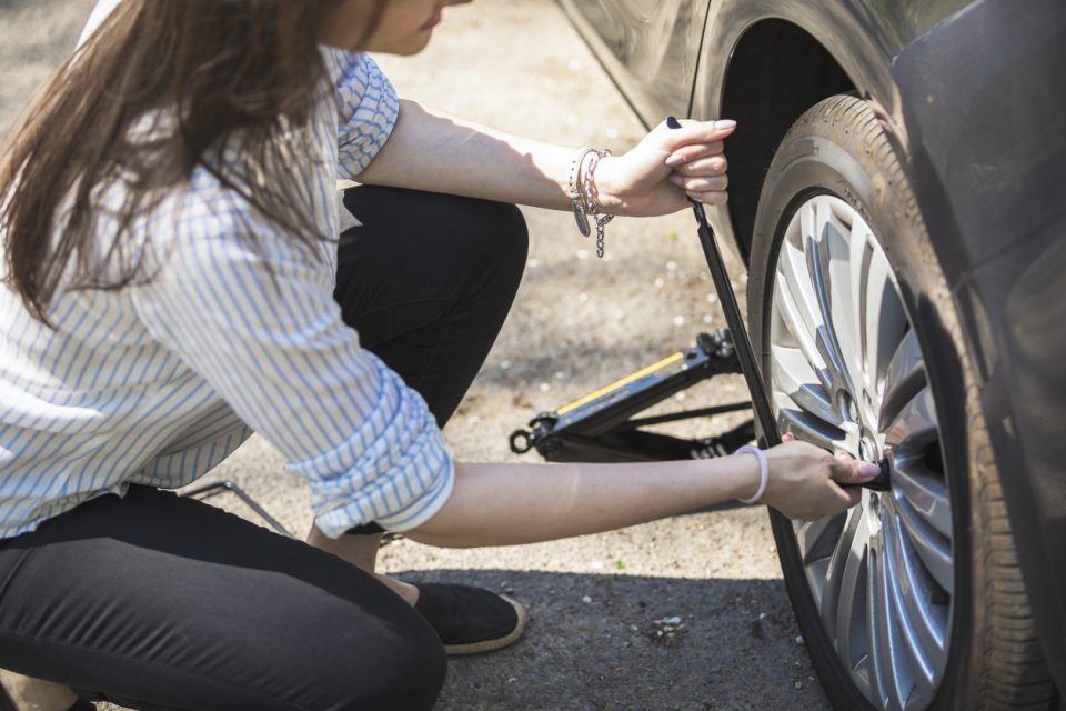 Woman changing a flat tire on the side of the road