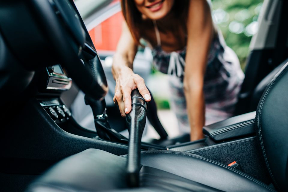 Happy woman cleans the interior of her car with vacuum cleaner.