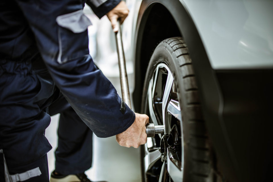 Close up of unrecognizable auto repairman using socket wrench while changing a tire in a workshop.