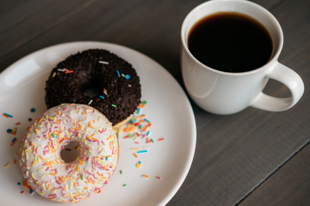 Black coffee in a white mug and two donuts on a plate.