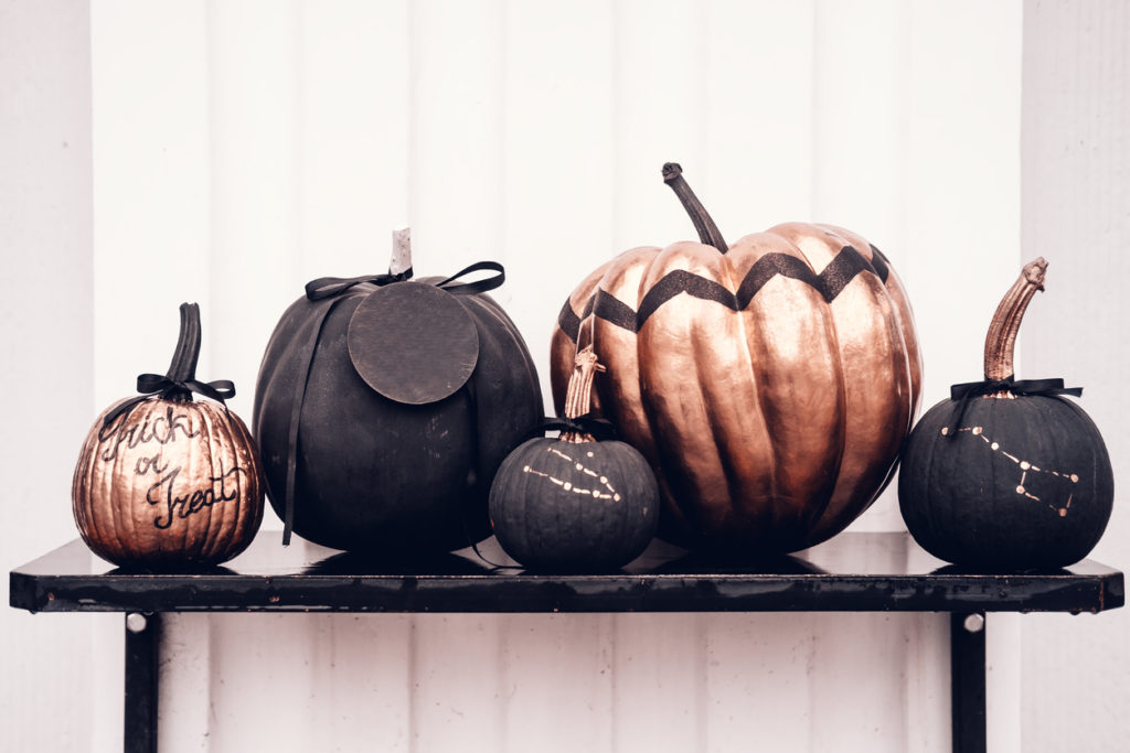 Black and rose cold colored pumpkins against white wall.