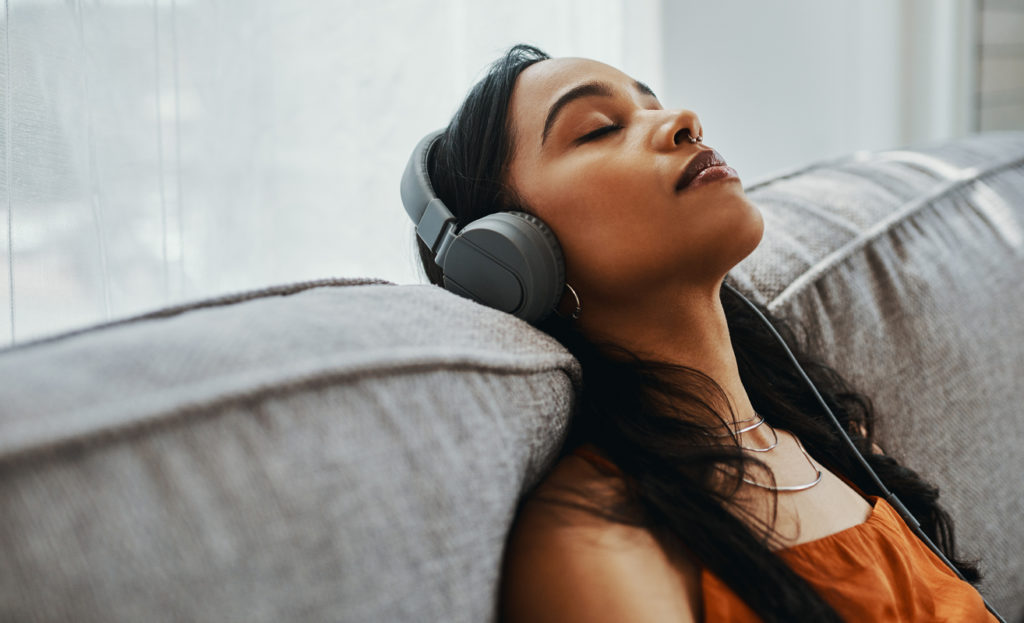 Young woman wearing earphones, listening to music on her couch