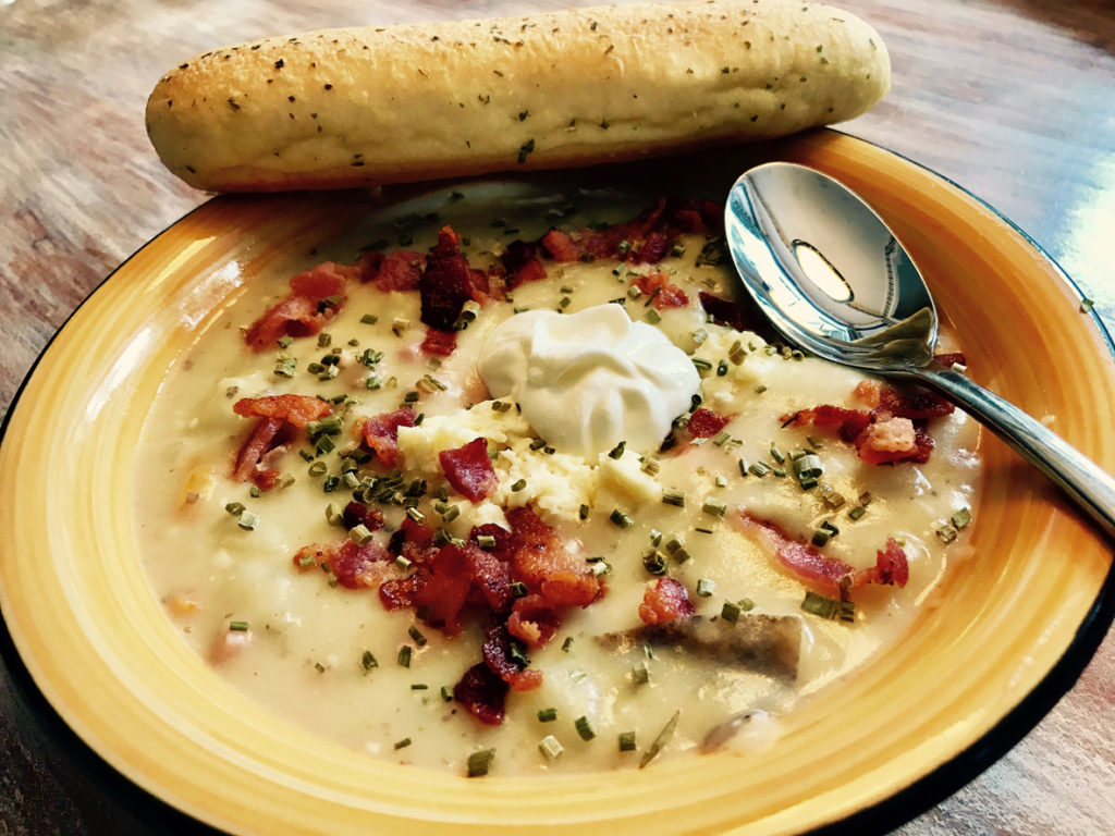 Close up of a bowl of Loaded Potato Soup with a bread stick.