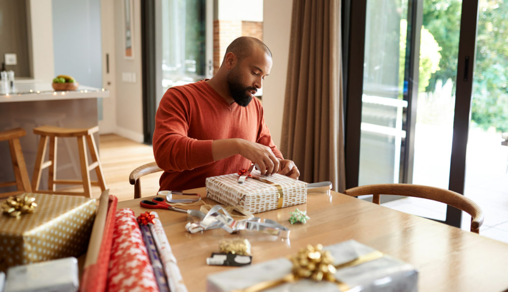 Shot of a young man wrapping Christmas presents at home