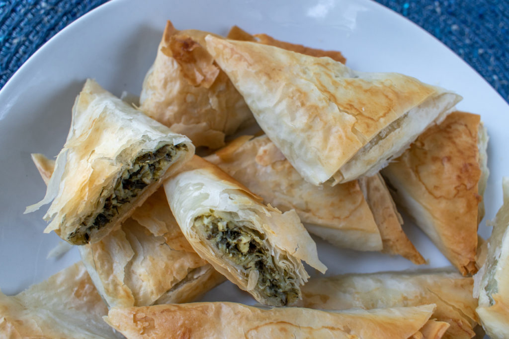 Spanakopita Greek Spinach puff pastry pie triangles on white plate.