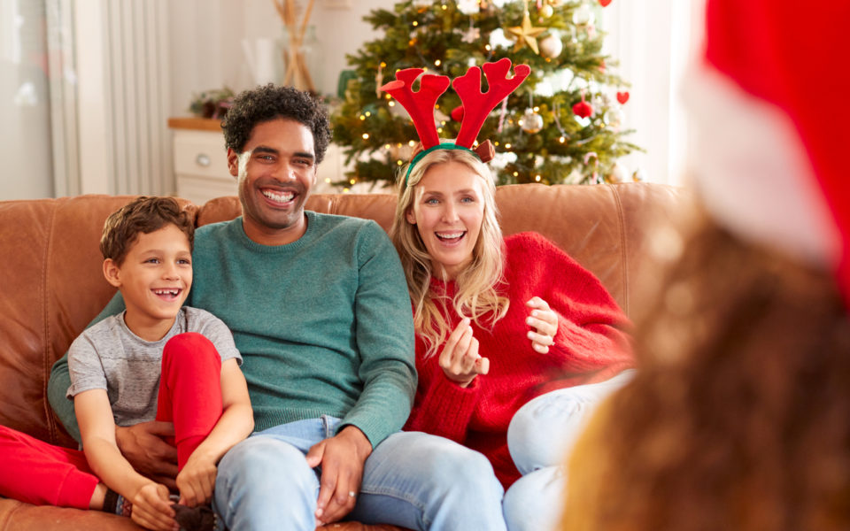 Family Sitting On Sofa Playing Game Of Charades At Christmas Together