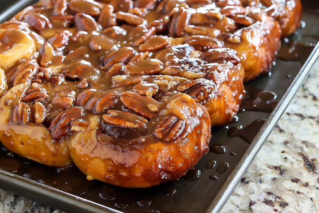 Cinnamon rolls with sticky pecan topping arranged on baking pan