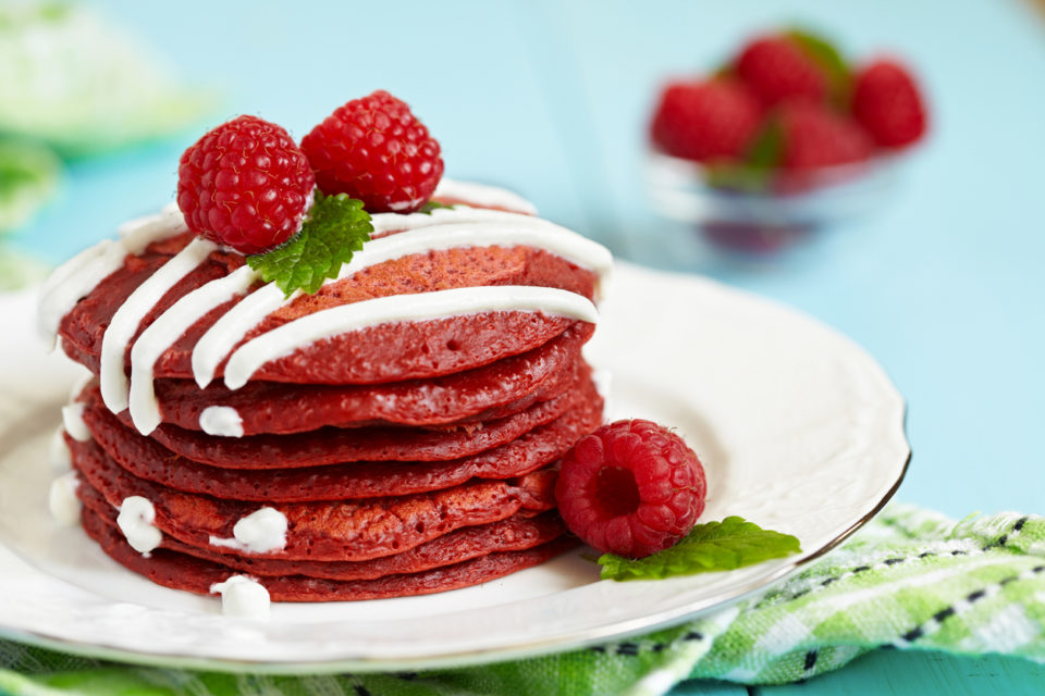 Stack of red velvet pancakes with icing and raspberries