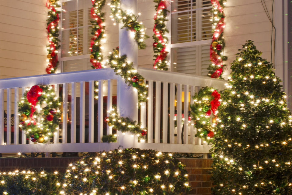 White Christmas lights, garland, and red bows decorating the front porch of a house