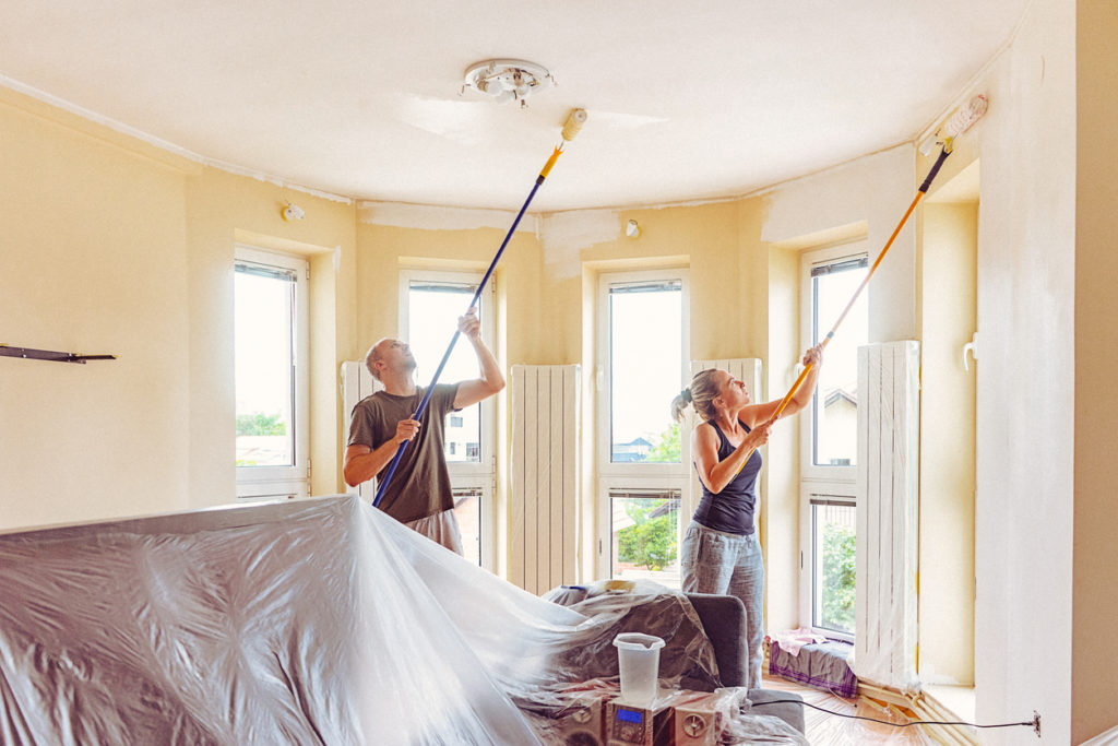 DIY home renovation work. Couple painting wall and ceiling with telescopic roller Man and woman in casual wear. The shot is executed with available natural light, and the copy space has been left.