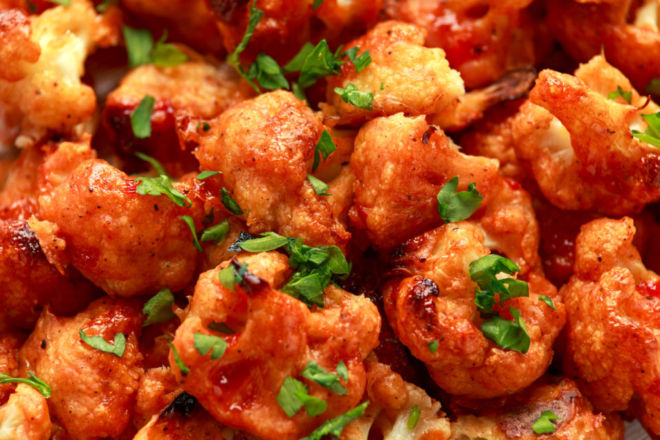 Vegan cauliflower buffalo wings on white wooden board.