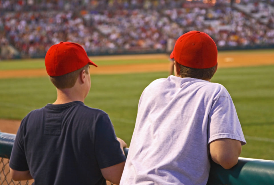 Two baseball fans a the stadium wearing a red cap