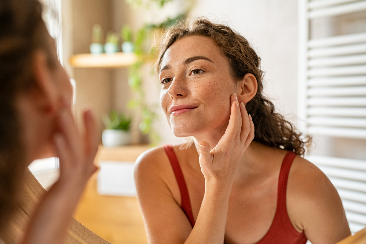 young woman looking in mirror at skin