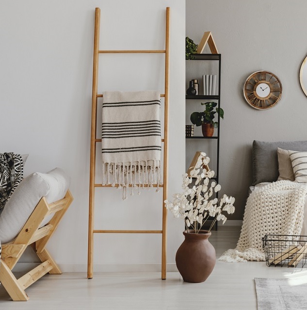 Blanket ladder leaning against a white wall of a bedroom with a white and black striped blanket