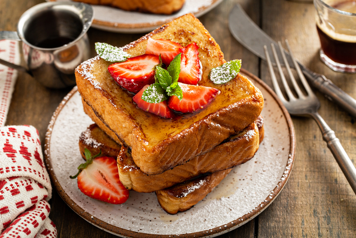 French toasts with strawberry and powdered sugar for breakfast on a wooden table