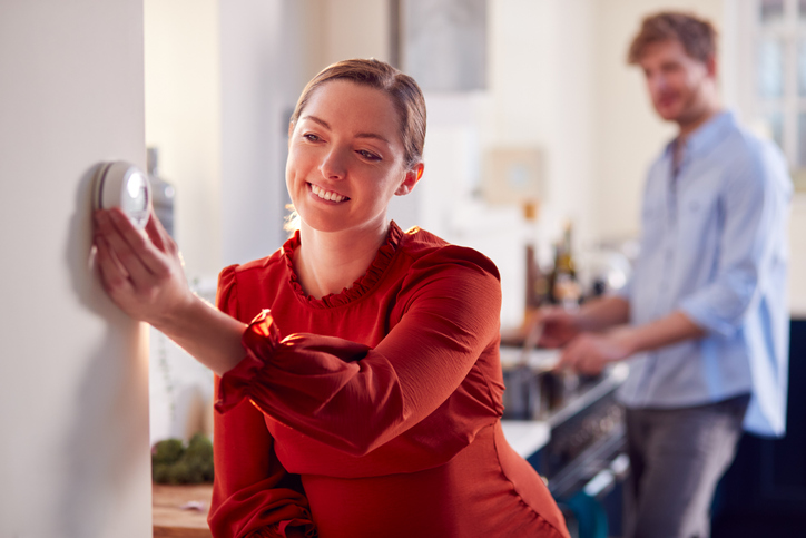 Couple With Woman With Prosthetic Arm Turning Down Heating Control In Kitchen Together