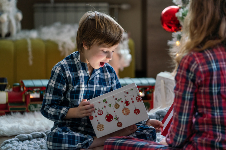 Surprised little boy opening Christmas present whit her sister at home