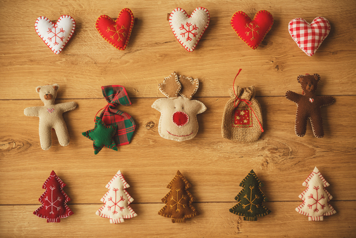 Stuffed linen ornaments in shape of hearts, teddy bears, reindeer, Christmas trees, and small sacks are arranged on table.
