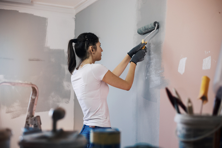 Young woman with hearing aid, during reconstruction of apartment, enjoying while painting her walls