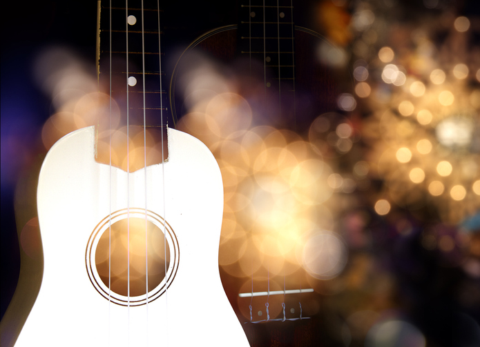 White acoustic guitar at front. Background is out of focus and lighting effect