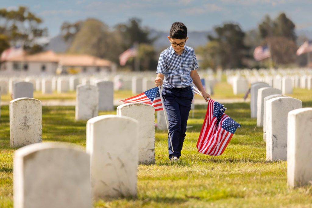 A young boy placing American flags on veterans graves at a veterans cemetery on Memorial Day.
